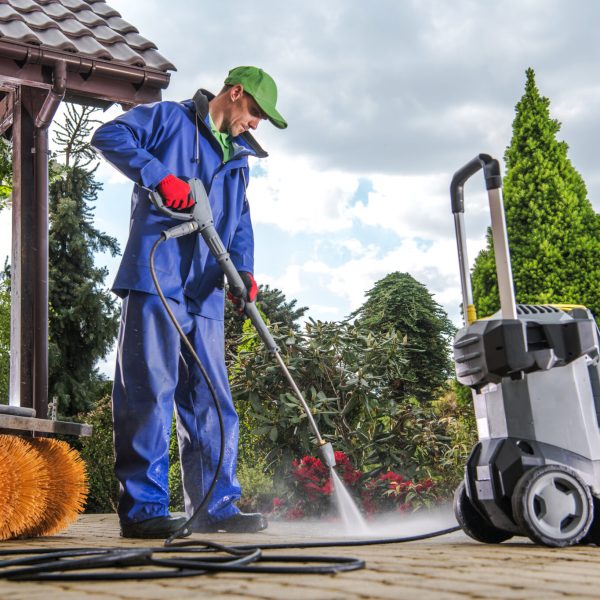 Caucasian Men Washing Residential Bricks Made Driveway and Paths Using Powerful Pressure Washer. Spring Maintenance Theme.